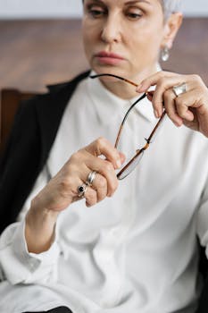 A contemplative woman holds glasses, suggesting deep thought or decision-making in a professional environment.