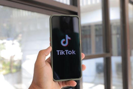 A hand holds a smartphone displaying the TikTok app in an indoor setting.