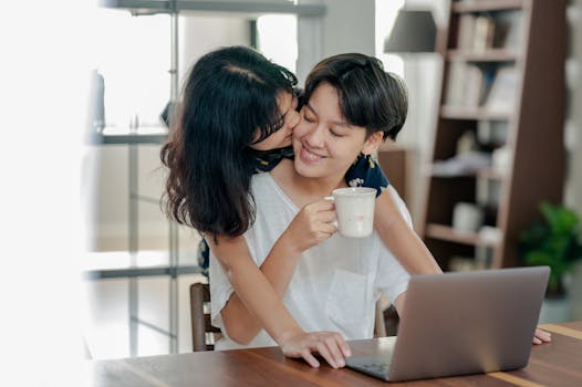 A happy couple embracing while working from home with a laptop and coffee.