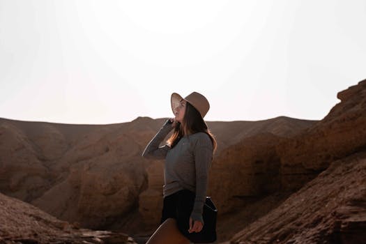 A woman in a hat explores a sunlit desert canyon at sunset, embracing adventure and nature.