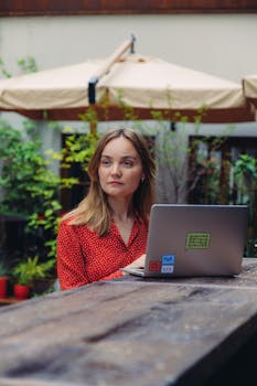 Female freelancer working on a laptop outdoors in a casual setting during summer.