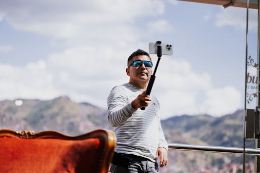 Man holding a smartphone on a selfie stick with mountains in the background in Cusco, Peru.