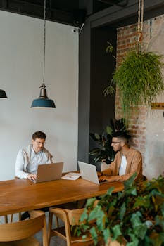 Two professionals collaborating in a modern coworking space with laptops.