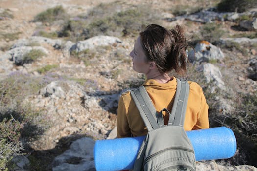 Woman sitting with backpack on rocky terrain, enjoying nature view.