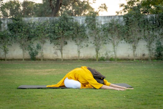 Adult woman performing yoga pose outdoors on a mat surrounded by green grass and trees.