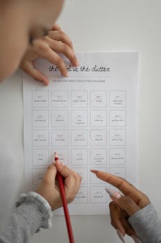 Hands using a red pencil to mark a declutter challenge sheet indoors.