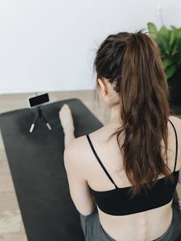 Woman practicing yoga indoors with a smartphone on a tripod for online content creation.