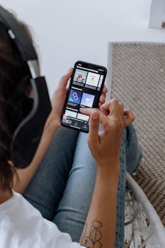 A close-up of a person relaxing indoors, using a smartphone and headphones to enjoy music.