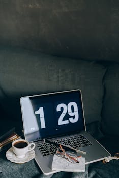 A cozy indoor workspace featuring a laptop, coffee cup, and eyeglasses on a couch.