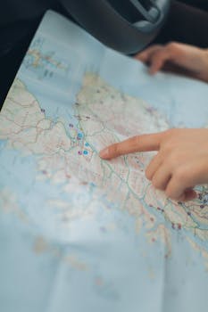 A woman's hand pointing at a location on a world map inside a car, highlighting navigation and travel planning.
