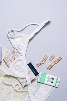 Flat lay of travel essentials including map, passport, smartphone, and bikini.
