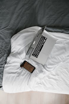 Minimalist overhead view of a laptop and smartphone on a cozy bed, ideal for remote work settings.
